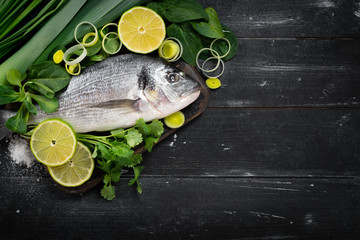 Fresh and raw dorada fish with lemon and herbs on a black wooden background, top view and copy space
