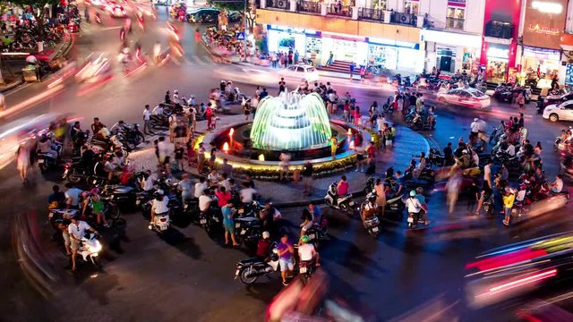 Time-lapse Aerial view, there are people and vehicles light trails crowd on busy intersection locating next to Hoan Kiem lake in old quarter of Hanoi capital at night..
