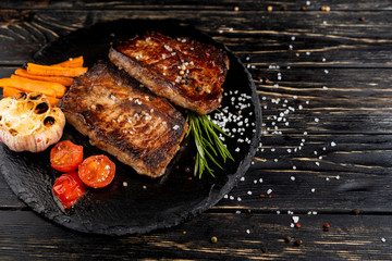 juicy piece of fried meat lies on a stone plate against a black wooden table