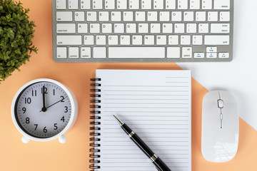 Directly above shot of office desk with potted plant, computer keyboard and mouse, note pad, alarm clock and pen on multicolored background.
