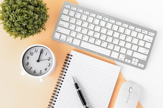 Directly Above Shot Of Office Desk With Potted Plant, Computer Keyboard And Mouse, Note Pad, Alarm Clock And Pen On Multicolored Background.