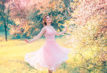 happy girl in short flying gentle pink dress laughs joyfully, doll princess whirls in bright yellow spring garden with flowering trees, positive emotions, movement in photo with creative colors