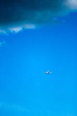Airplane flies under thundercloud in bright blue sky