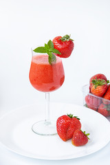 Strawberry smoothie in a glass on a high leg decorated with strawberries and mint on a white background. Strawberry season.Healthy lifestyle.
