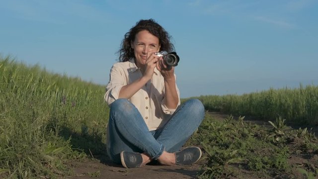 A female photographer takes pictures in nature. Pretty woman with a camera in the field.