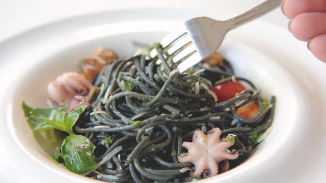 Italian food serving. Hand twirling squid ink pasta with seafood and cherry tomatoes on fork