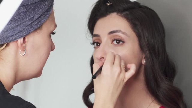 Closeup timelapse shot of cute young female makeup artist enjoying working with a beautiful young mixed race brunette model with vintage hairstyle, applying fresh trendy makeup on her face using