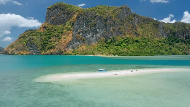 Aerial drone footage circling a sandbar form distance. Beautiful Lagen Island and white cloudscape in background. El Nido, Palawan, Philippines