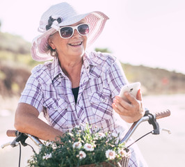 Happy senior adult woman stops pedaling to answer the mobile phone. Enjoying freedom outdoor with a...