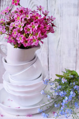 Heap of white crockery and pink field flowers on top. Interior idea