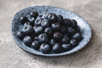 Obraz na płótnie Canvas Fresh Organic Blueberries in Gray Plate on Dark Stone Background