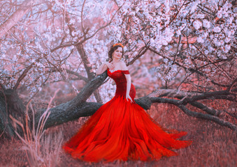 charming nymph sits on fallen tree in spring forest, lady in gorgeous red scarlet long dress with...