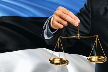 Estonian Judge is holding golden scales of justice with Estonia waving flag background. Equality...