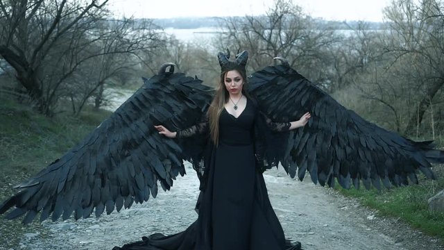 dark devil came down from heaven, girl with massive black wings and horns in long vintage dress with cool loose sleeves fell into trap, mythical creature looks into eyes of danger and her own death