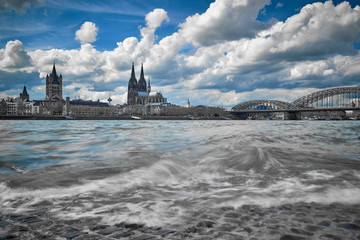 Panorama Kölner Dom und Blick auf die Altstadt St Martins Kirche und Hohenzollernbrücke. Stadtansicht Köln Schwarz Weiss mit Blick über den Rhein mit Wellen Blauer Himmel teilweise bewölkt.