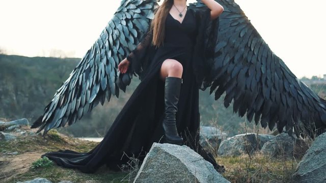 charming gorgeous dark goddess controls wind, waving hem and long train of black dress with wide lace sleeves, lady with sharp horns and black feather wings ready to fly into sky, creative image