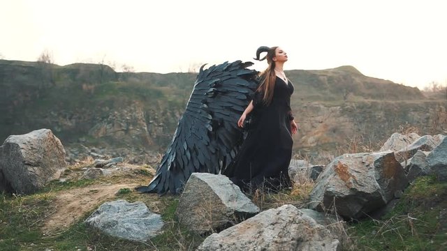 angel of death gathers with forces to start war, girl in black long vintage dress with lace sleeves alone beside large lake, lady with strong feather wings down on ground and horns on her head