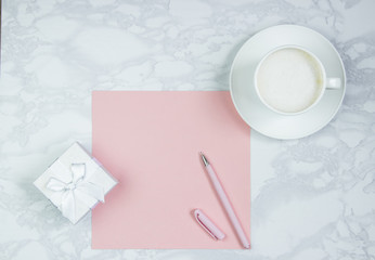 Obraz na płótnie Canvas Pink sheet of paper, pink pen, cup of coffee and gift boxes on the table. Pink blank card, sheet for writing. Layout for adding inscriptions. Top view, flat lay, copy space