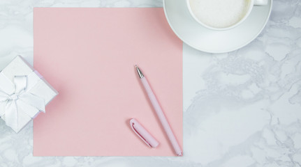 Pink sheet of paper, pink pen, cup of coffee and gift boxes on the table. Pink blank card, sheet for writing. Layout for adding inscriptions. Top view, flat lay, copy space