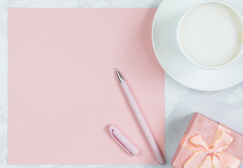 Pink sheet of paper, pink pen, cup of coffee and gift boxes on the table. Pink blank card, sheet for writing. Layout for adding inscriptions. Top view, flat lay, copy space