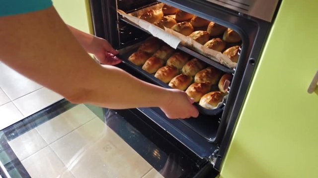Woman takes out tray with many traditional delicious baked pasties from hot oven in bakery. 4K clip