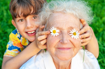 Laughing grandson with his beloved grandmother spend leisure time outdoors. The boy puts his...