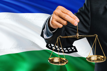 Judge is holding golden scales of justice with Lesotho waving flag background. Equality theme and...