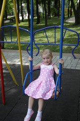 girl in a pink dress in white large polka-dot riding on a swing