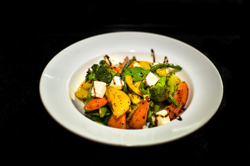 a white plate setup showing a delicious home made salad consisting of a variety of  vegetables like capsicums, cottage cheese, broccoli, tomatoes, baby corns etc served with a sauce dressing