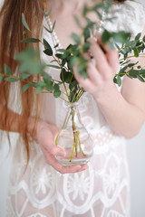 Fototapeta na wymiar The hands of a young girl hold eucalyptus branches that are inserted into a glass vase that is transparent to a small vase. Eucalyptus branches and girl's hands