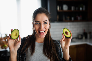 Beautiful smiling young woman preparing healthy food holding avocado