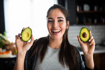 Beautiful smiling young woman preparing healthy food holding avocado