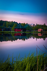 Small village red house with smoke reflects in clearly still water at evening