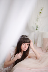 Naklejka premium Photo of a young girl in the style of fine art. Close-up portrait of a girl with a diadem in her hair that rests with her hands on a beautiful romantic bed. Girl dreams