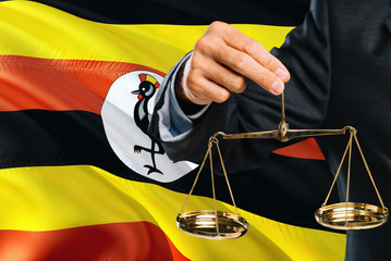 Ugandan Judge is holding golden scales of justice with Uganda waving flag background. Equality...