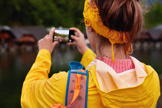 People, leisure, lifestyle and technology concept. Female traveler stops near scenic view, explores nature holds mobile phone, wears yellow anorak, focus on hands with modern electronic device.