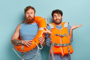 Serious male swim instructor with lifeline, doubtful trainee wears orange vest, spreads hands,...
