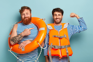 Glad proud male swimmer raises arm and shows muscle, ready for saving people life on water, wears...