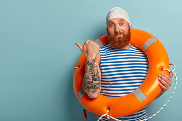 Photo of puzzled male swimmer or instructor points thumb left, attracts your attention to copy...