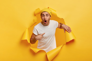 Who, me? Stupefied emotional man points at himself, dressed in casual white t shirt, keeps mouth...
