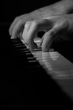 A young pianist practices in this black and white photograph with isolated hands on a piano keyboard
