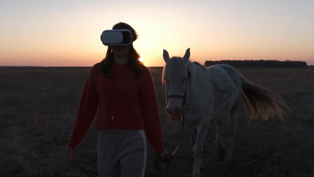 Pretty girl in glasses virtual reality leads white horse across the dried field