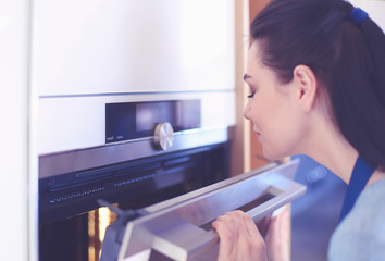 Beautiful young woman checking how her cake is doing in the oven