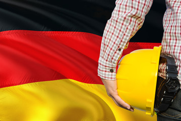 German Engineer is holding yellow safety helmet with waving Germany flag background. Construction...