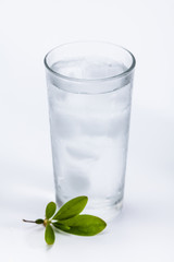Glass of cold ice water with green leaf on white background