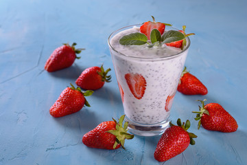 Healthy and tasty yogurt detox smoothie with chia seeds and pieces of ripe strawberries in a glass on a blue background next to some few strawberries