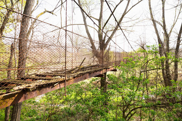 An abandoned rusty metal iron bridge construction crossing over the wild and green vegetation