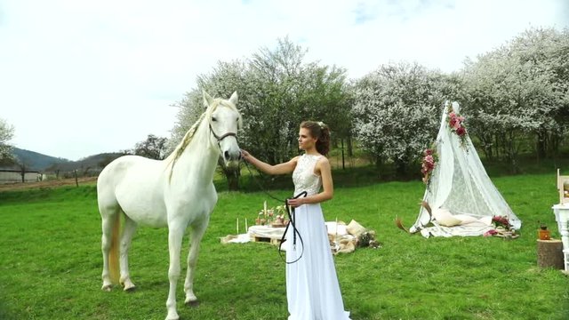 White horse in wedding day outside with bride and groom and caressing jipo head wedding teepee making background in nature.