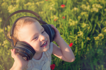 Happy smaill girl listen to the music in the earphones. Child walking in the field of poppy flowers