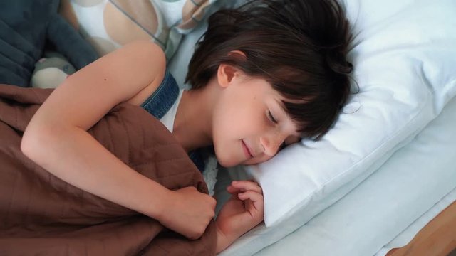Little girl sleeps sweetly in bed, wakes up and stretches, slow motion